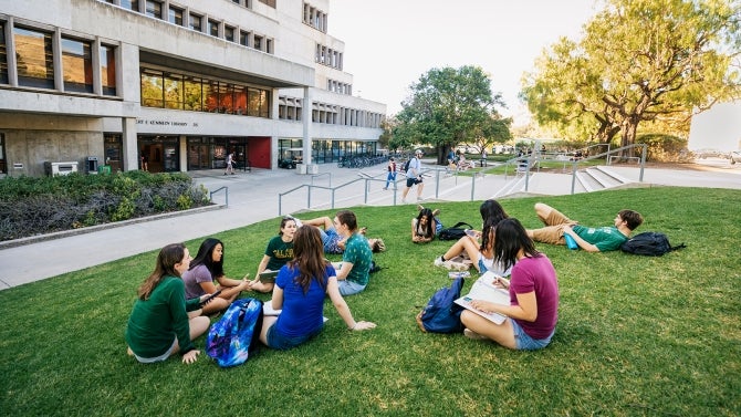 Students sit on front lawn of library